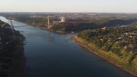 Triple-border-between-Argentina,-Brazil-and-Paraguay,-intersection-bridge-of-the-Parana-and-Iguazu-Rivers-at-sunset---Aerial-wide-shot