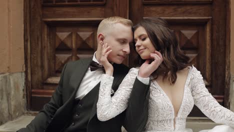 newlyweds love, caucasian groom with bride sitting, embracing, hugs in city street, wedding couple