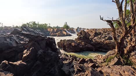 rocky landscape with cascading waterfalls under bright daylight at khone phapheng falls, showcasing natural beauty and rugged terrain