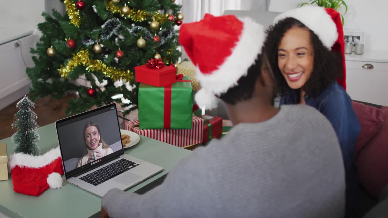 pareja afroamericana con sombreros de santa haciendo una videollamada en una computadora portátil en casa durante la navidad