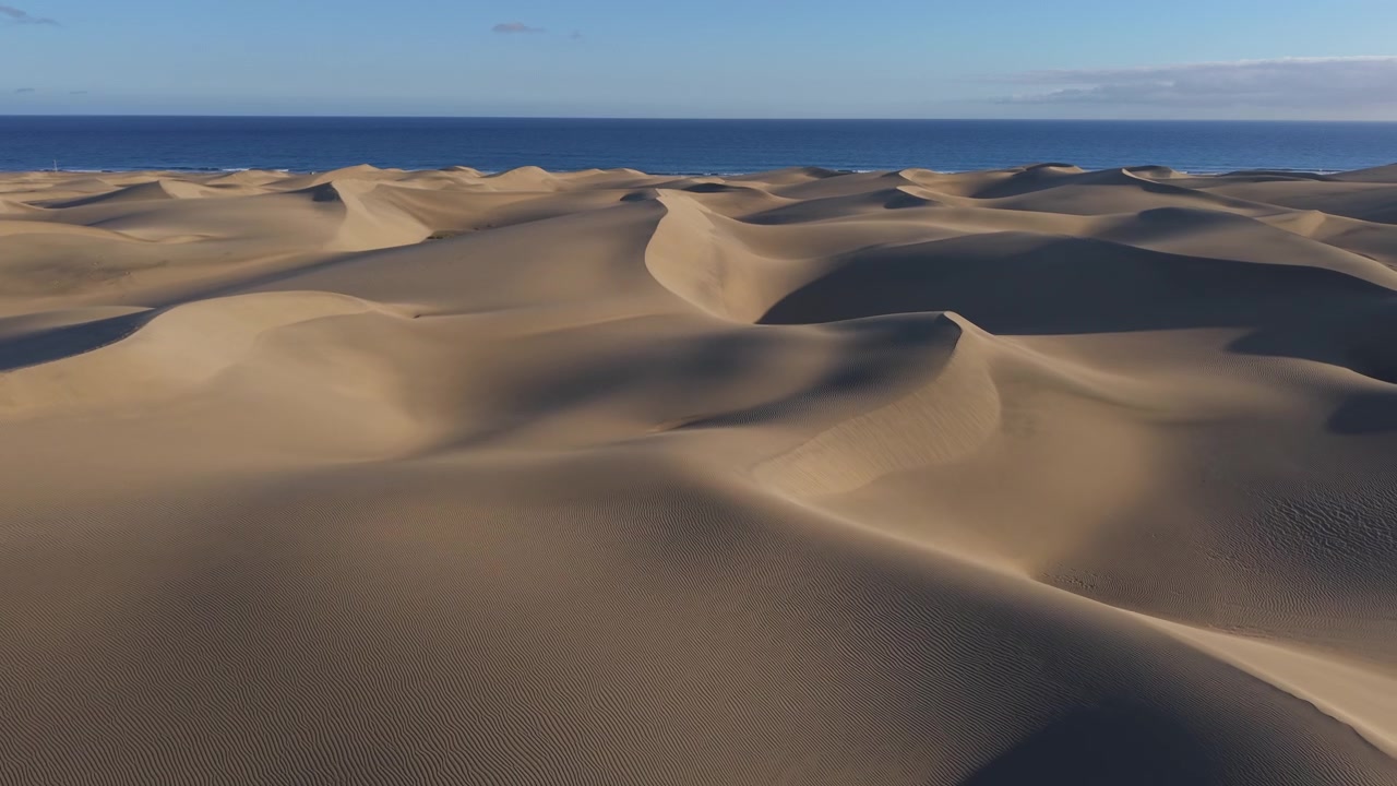 Hermosa vista aérea volando sobre las Dunas de Maspalomas, un impresionante paisaje desértico en Gran Canaria, con el azul del océano Atlántico visible.