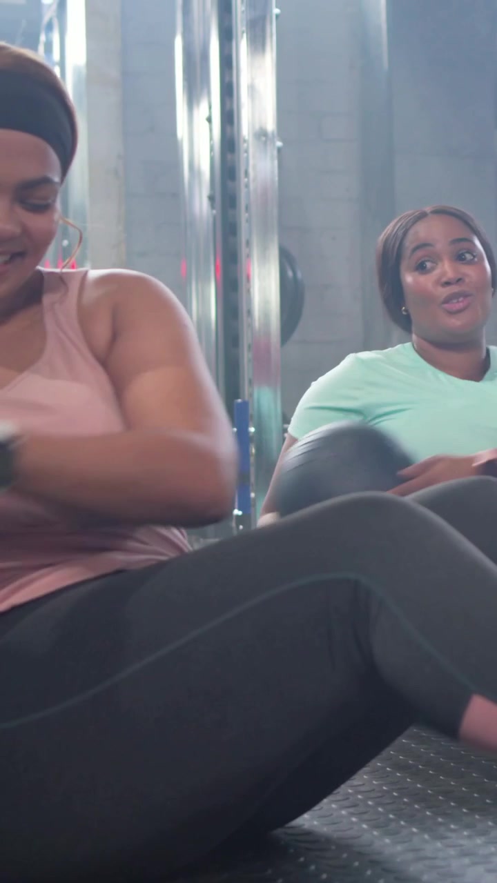 Vídeo vertical: Iniciando rotina, mulher de regata rosa girando no colchonete de ginástica passando bola medicinal para o core