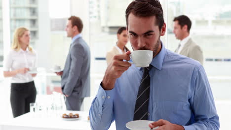 Hombre-De-Negocios-De-Pie-Y-Tomando-Un-Café-Con-Sus-Colegas-Detrás