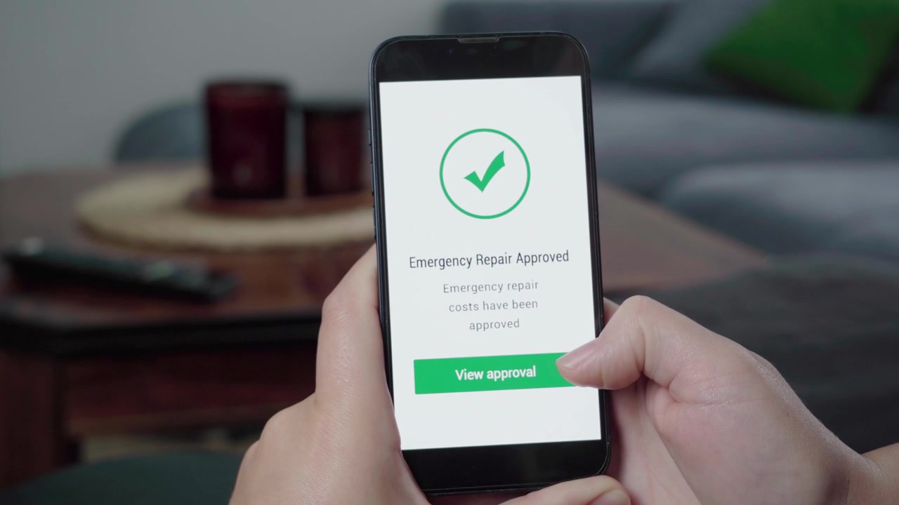 Mani che utilizzano un telefono cellulare che mostra un messaggio di approvazione dei costi di riparazione di emergenza con una grande icona di spunta e un pulsante per visualizzare l'approvazione.