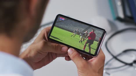 Zusammensetzung-Eines-Männlichen-Arztes,-Der-Ein-Rugbyspiel-Auf-Dem-Smartphone-Beobachtet