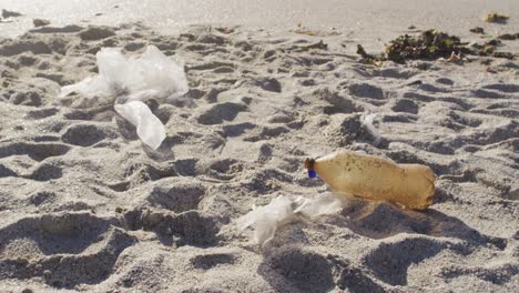 close up of plastic bottle and rubbish lying on empty dirty beach