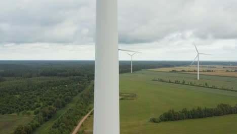 upward aerial close up of a rotating wind turbine with wind turbine park in the background