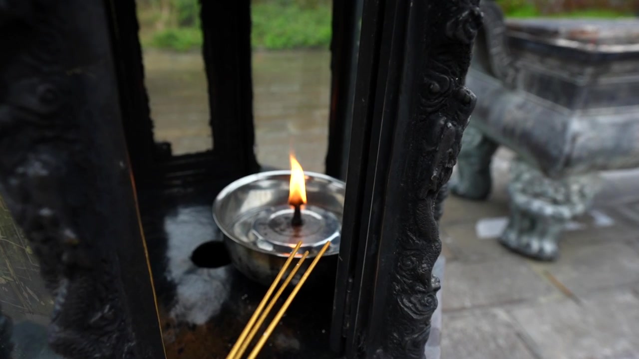 Close up of a person lighting incense sticks from an oil lamp flame at a Buddhist temple