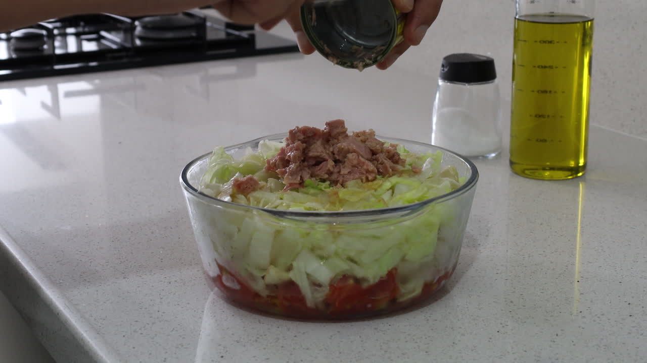 Close-up of fresh cabbage and tomato salad in a glass bowl as canned tuna is being added on top, emphasizing healthy and protein-rich meal preparation
