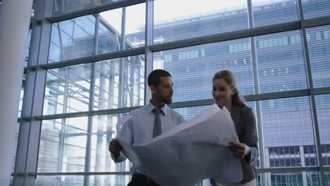 male and female architects discussing over blueprint in office 4k