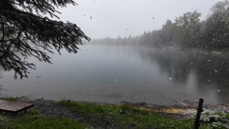 big snow flakes are falling on lake with bench next to it