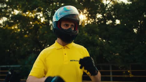 portrait of a motorcycle driving instructor in a yellow t-shirt who takes off the protection from a motorcycle helmet and looks to the side