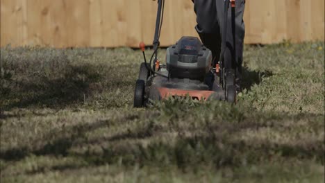 an electric mower being pushed over grass and weeds towards the camera