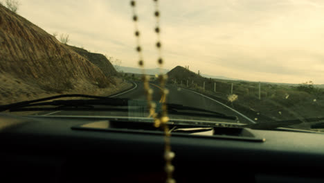 rosary cross swinging off car mirror while driving on route 66 at sunset