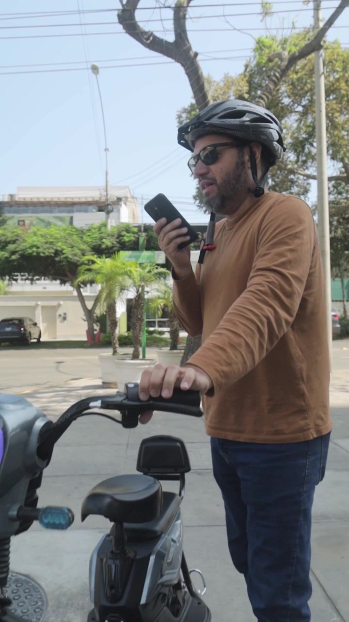 Man with Helmet and Sunglasses Talking on Smartphone Next to Electric Scooter