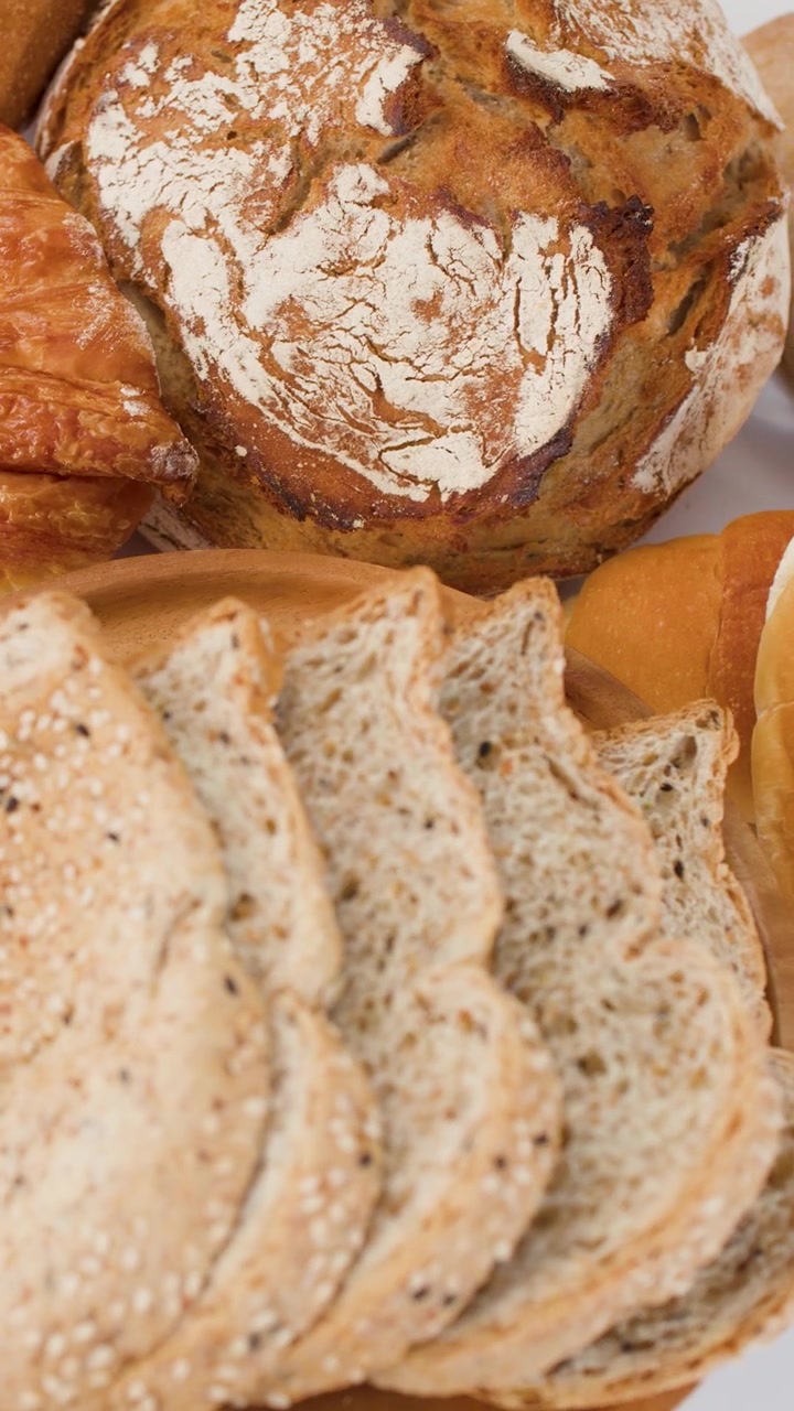 Primo piano dall'alto di pane multicereali a fette, pane a lievitazione naturale e croissant su un piatto di legno.