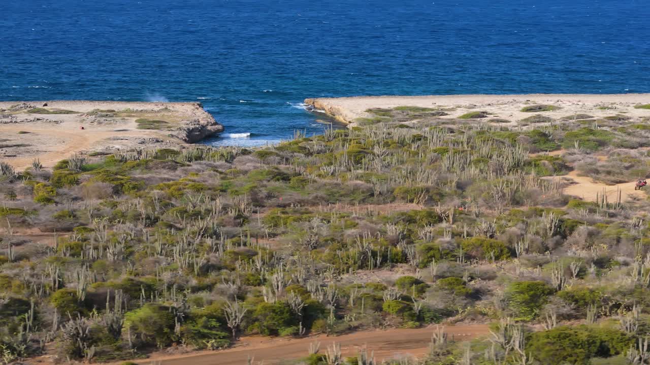 Aerial panoramic overview of UTV riders along the rugged north coast of Curacao with its rocky shoreline and blue ocean waves crashing below on sunny day