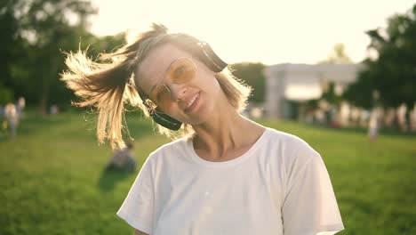 a sunny day in the park. a girl with two tails on her head listens to music on headphones and has fun. dancing, posing in front