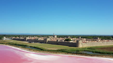 the historical town of aigues-mortes in the camargue, france during a sunny summer day which is located next to a pink salt lake