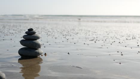 rock balancing on ocean beach, stones stacking by sea water waves. pyramid of pebbles on sandy shore