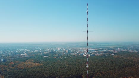one telecommunication tower is located near the city in the background of the forest. camera motion back