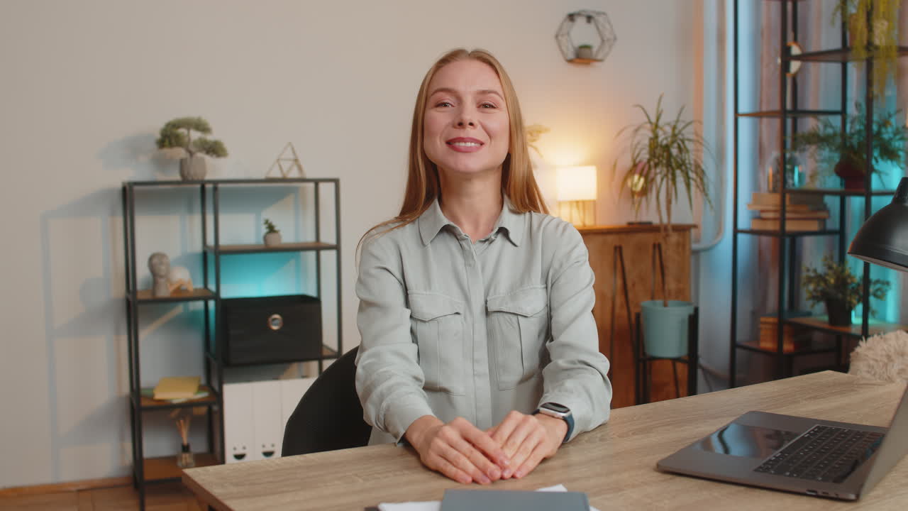 Portrait of happy caucasian businesswoman employee waves hand hi gesture greeting at camera at desk