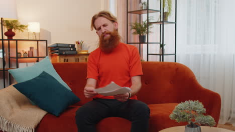 stressed redhead man looking at unpaid bank debt loan, doing paperwork planning budget, throws bills