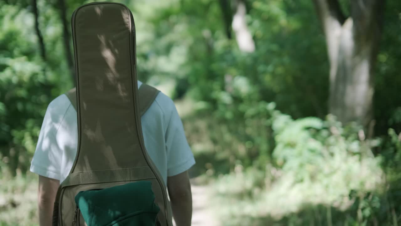 숲 근처의 거리에서 기타를 들고 는 젊은 남자