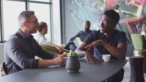 two happy male creatives talking at a table in their workplace cafe, close up