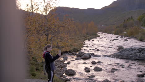 a woman takes a photo next to a picturesque river in norway in the fall, slow motion