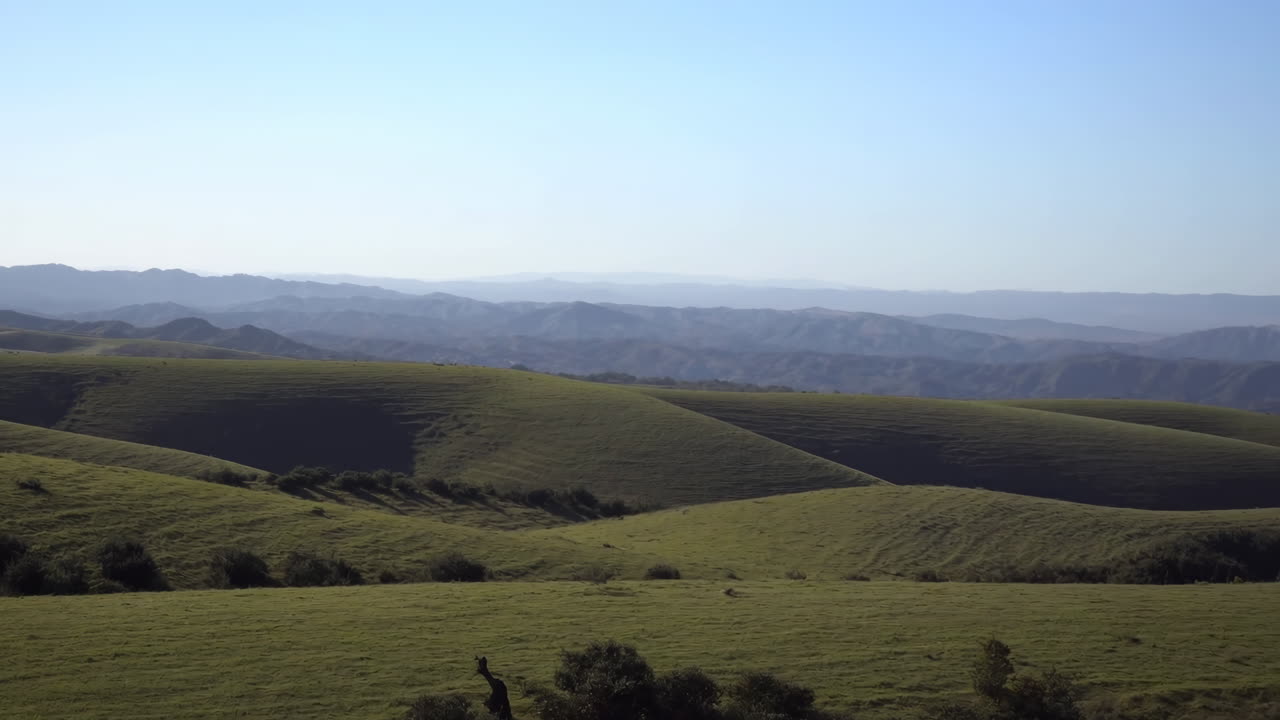 Dolci colline verdi e montagne distanti sotto un cielo azzurro limpido