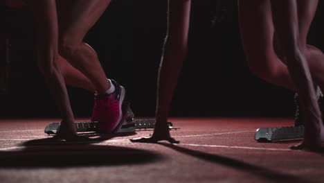 tres atletas deportivas por la noche en la cinta de correr comienzan la carrera a la distancia de sprint desde la posición sentada