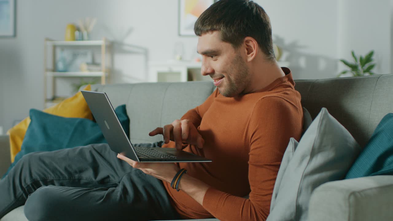 Man Lying on His Sofa At Home, Uses Laptop with Green Mock-up Screen. Over The Shoulder Shot of Anonymous Man in the Living Room. In Slow Motion.