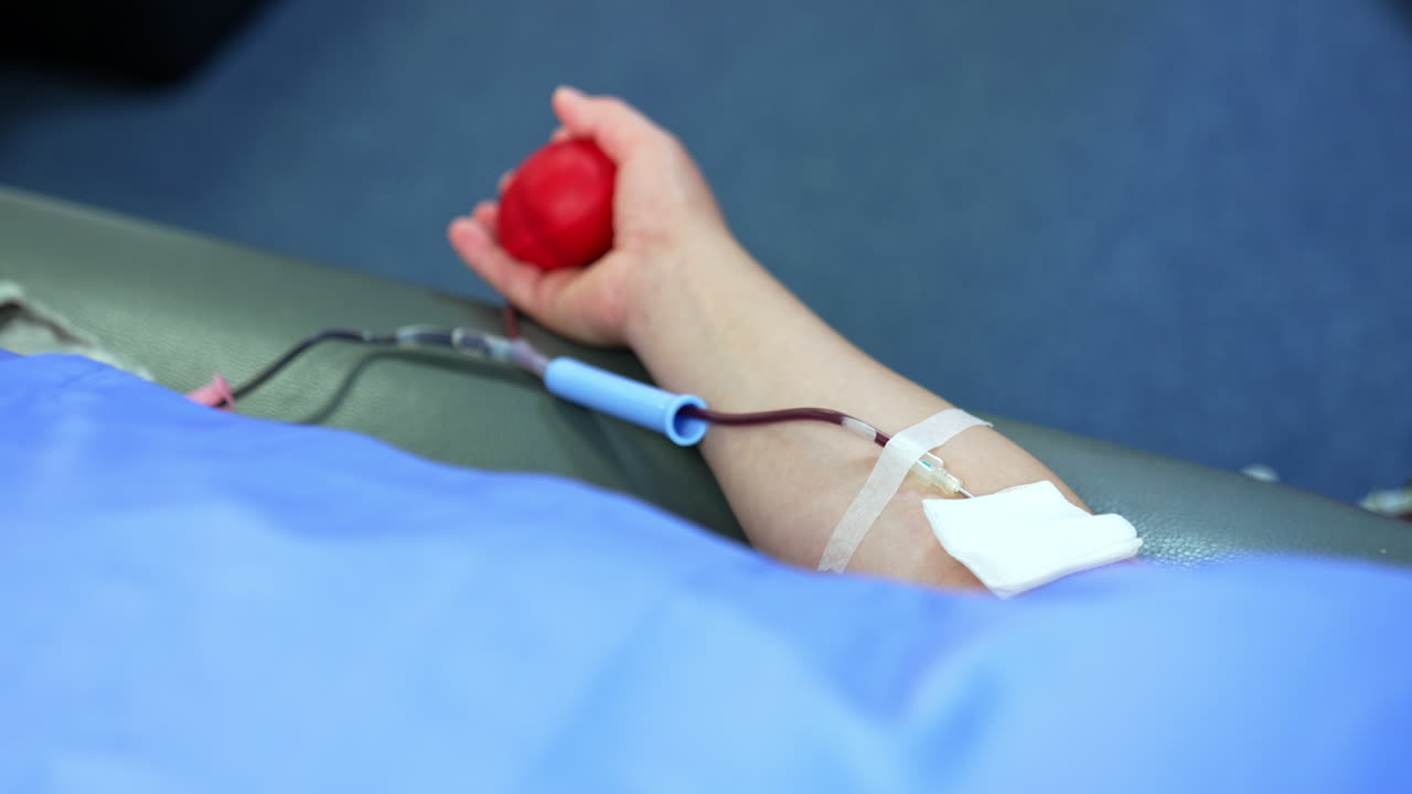 Arm of a person donating blood. A catheter is attached to the forearm filled with blood. Close up.