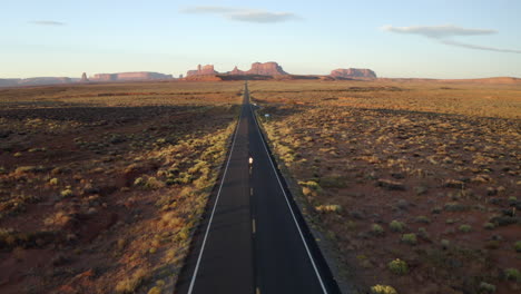 Drone-footage-of-man-walking-in-monument-valley,-along-empty-forest-Gump-highway-in-Utah