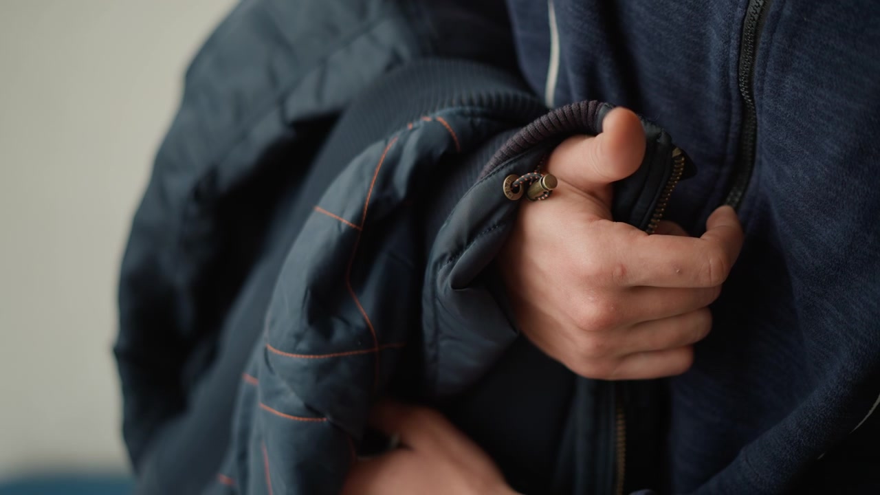 Primo piano di una persona che tiene la manica e l'area della cerniera di due giacche blu scuro, concentrandosi sulla presa della mano e sulla texture del tessuto. Il soggetto indossa una giacca mentre ne afferra un'altra con cuciture visibili.