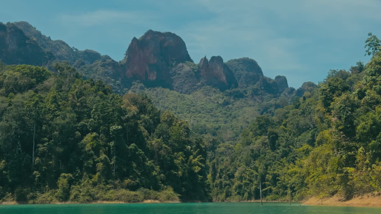 Những ngọn núi đá vôi hùng vĩ vươn lên trên rừng nhiệt đới tươi tốt tại Vườn Quốc gia Khao Sok, Thái Lan, thể hiện cảnh quan nhiệt đới ngoạn mục, thảm thực vật xanh tươi rậm rạp và vẻ đẹp hoang sơ nguyên sơ.