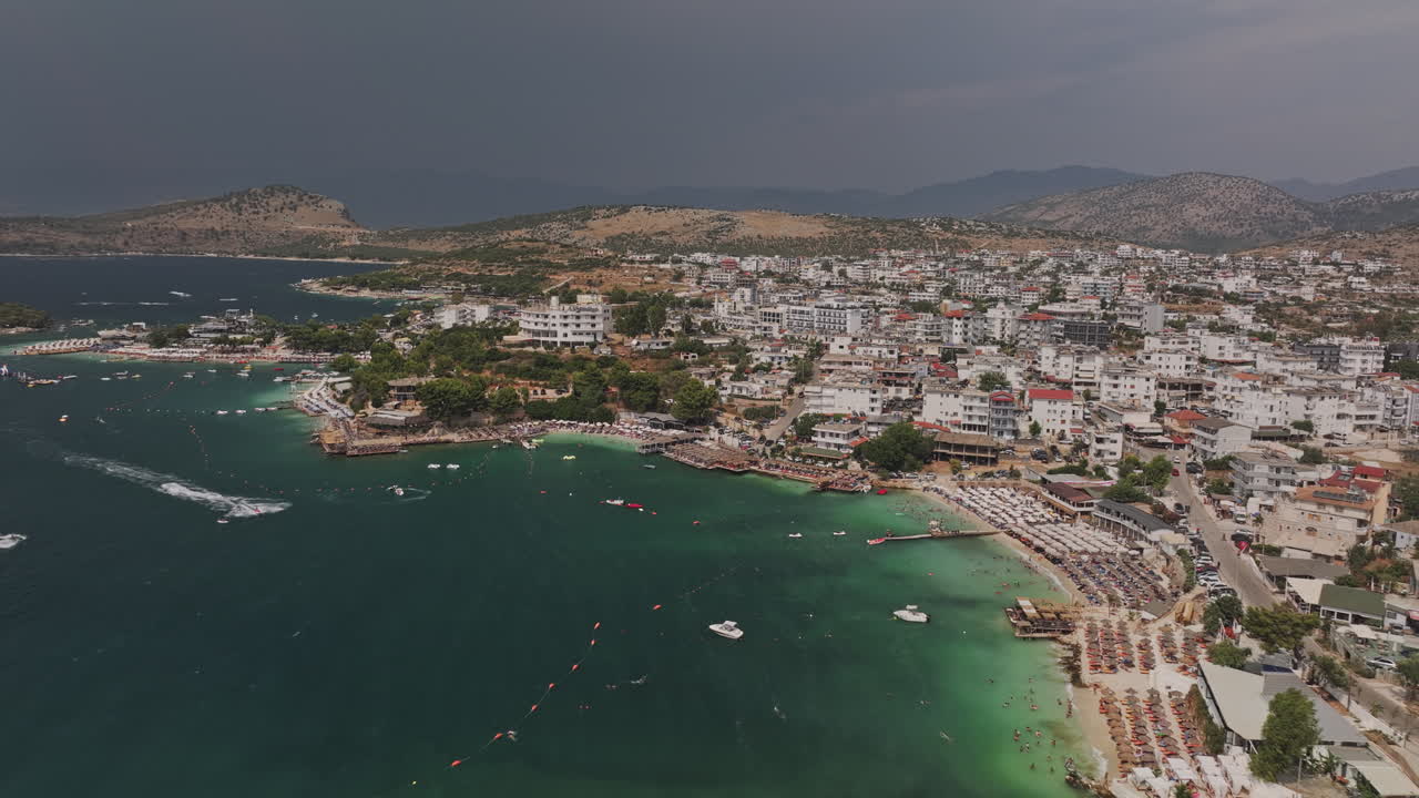 Ksamil Arnavutluk Aerial v3’ten, yazın tatil otellerini, plaj kulüplerini ve yamaç şehir manzarasını yakalayan el değmemiş turkuaz suların üzerinden geçiş – Mavic 3 Pro Cine ile çekildi – 18 Temmuz 2024