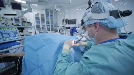 sala de operaciones, el paciente está bajo anestesia profunda, el cirujano con asistente utiliza los últimos dispositivos, método de plasma frío, cortes hinchazón en la garganta, el médico trabaja con una nueva sonda, lámpara frontal médica, lupas quirúrgicas
