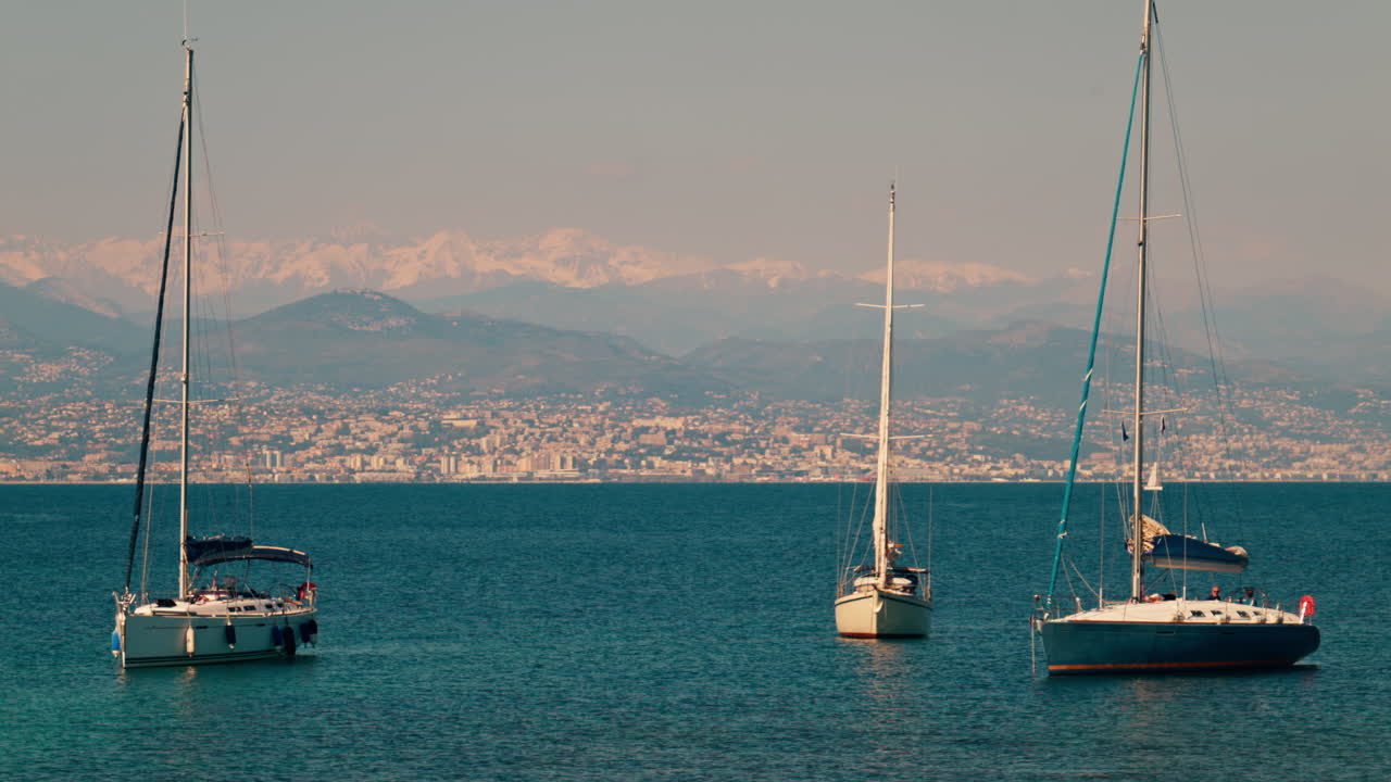 Barche che galleggiano sul mare con gli edifici e le montagne della Costa Azzurra sullo sfondo