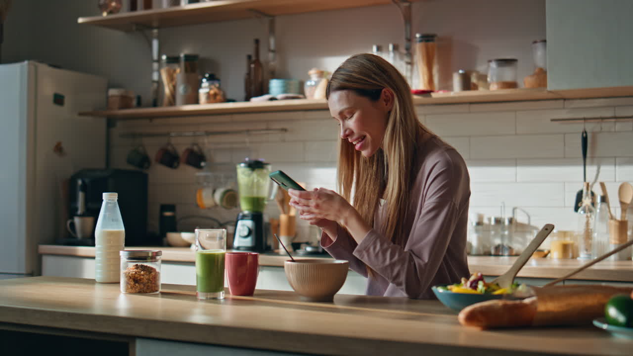 Smiling cook looking smartphone message in kitchen. Woman watching cellphone