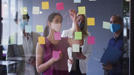 diversos colegas de negocios con máscaras faciales de pie haciendo lluvia de ideas en la oficina