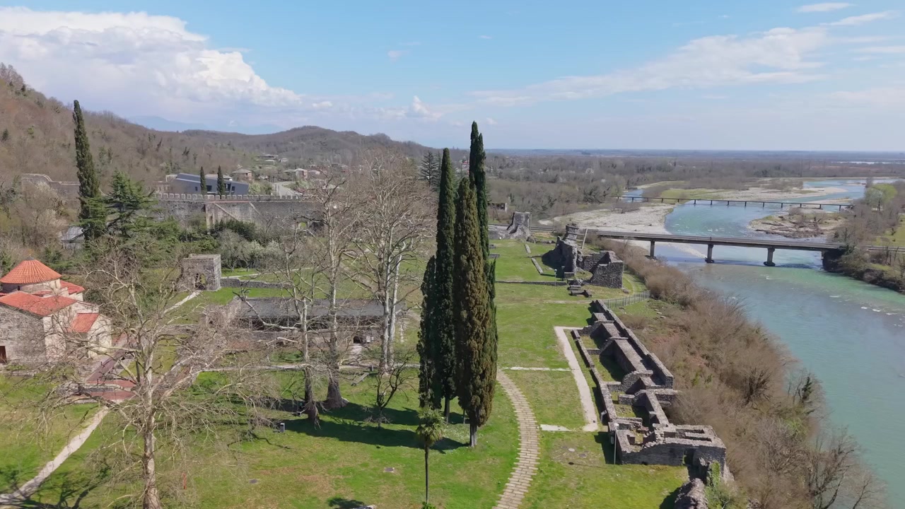 Filmato laterale con drone che cattura la Fortezza di Nokalakevi mentre rivela il fiume che scorre nelle vicinanze, circondato da una vegetazione lussureggiante, colline e il paesaggio scenografico della Georgia occidentale.