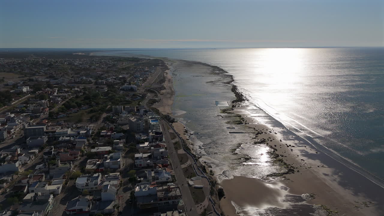 Experience a breathtaking aerial perspective of Las Grutas, Argentina, capturing the warm glow of sunset over Golfo San Matias, highlighting sandy shores and glimmering water.