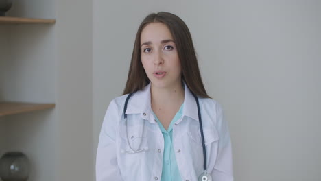 Smiling-young-female-doctor-wear-white-uniform-stethoscope-consulting-online-patient-via-video-call-looking-at-camera-speaking-cam-do-distance-video-chat-telemedicine-and-e-health-concept-webcam