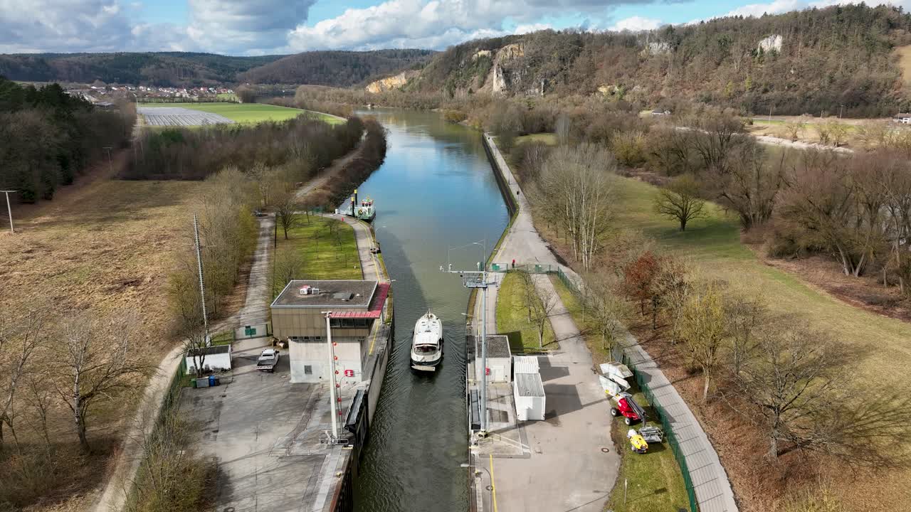A drone view of the Danube Canal, with a boat traveling and another one moored. The shot is set against a backdrop of beautiful hills and green fields
