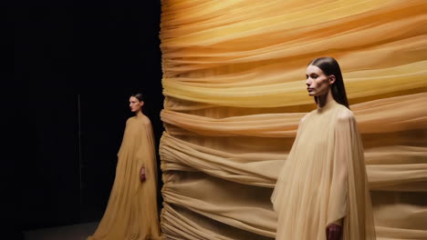 elegant models in flowy yellow gowns against draped backdrop