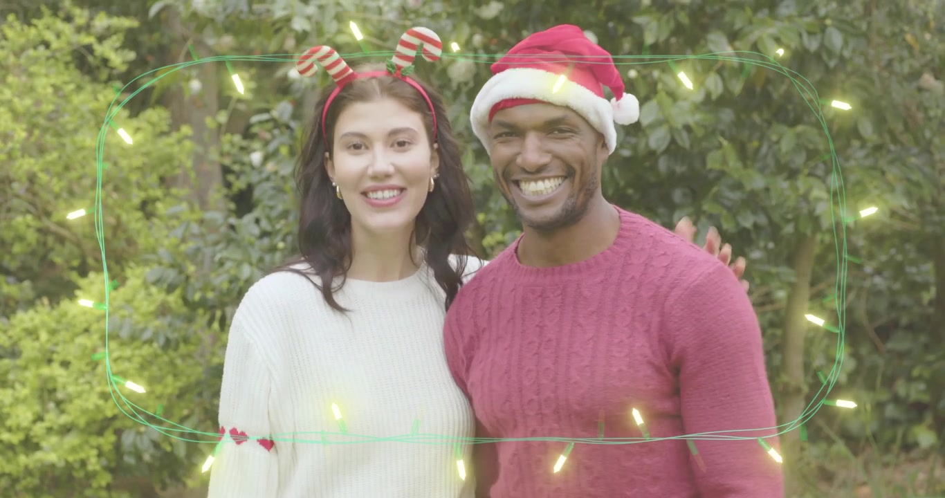 Işıklı süslemelerle çevrili bahçede el ele tutuşan çift, kadın bayram reklamı için Noel şapkası takıyor