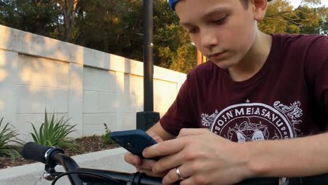 young boy riding a bicycle and using his smartphone outdoors