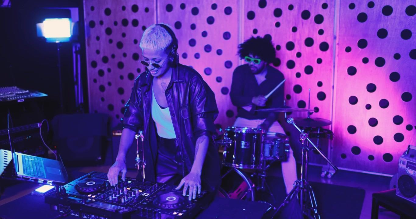 DJ donna e batterista si esibiscono dal vivo in uno studio musicale illuminato al neon.